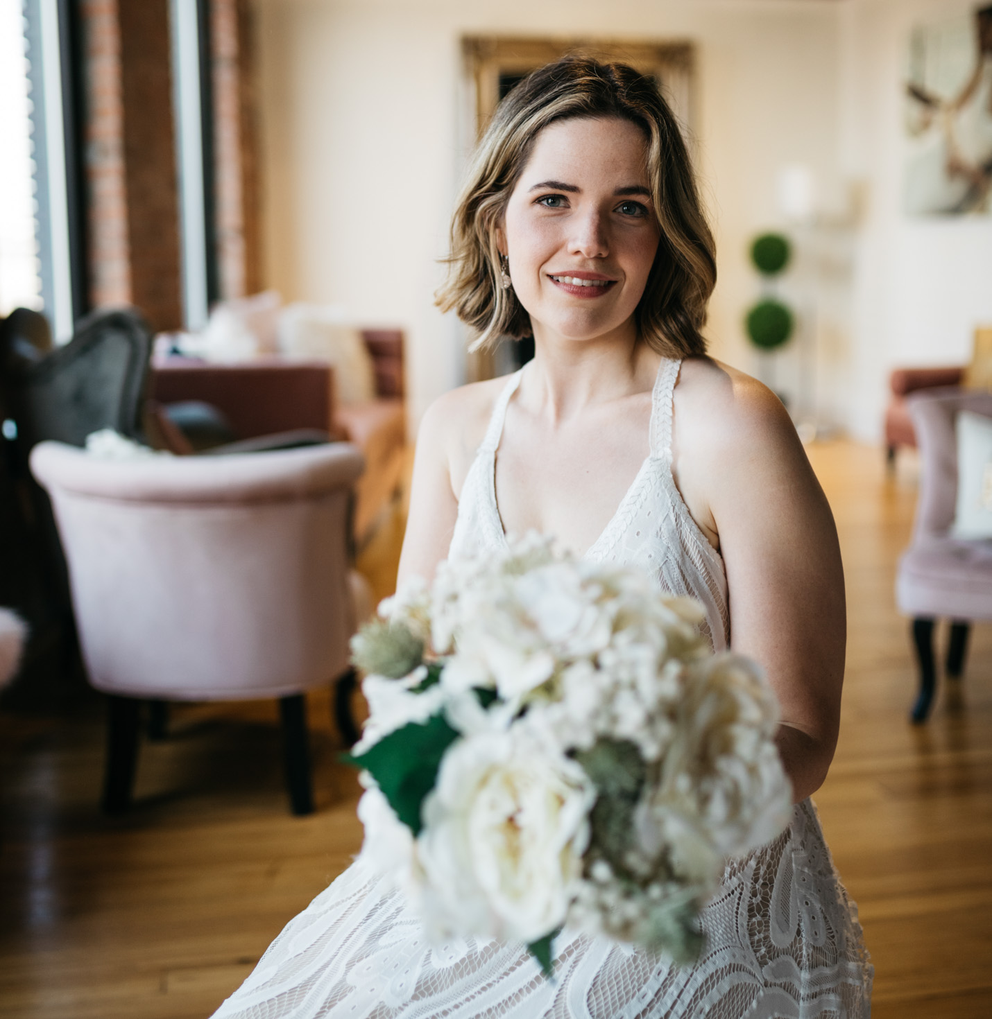 A bride trying on a dress while also holding flowers.