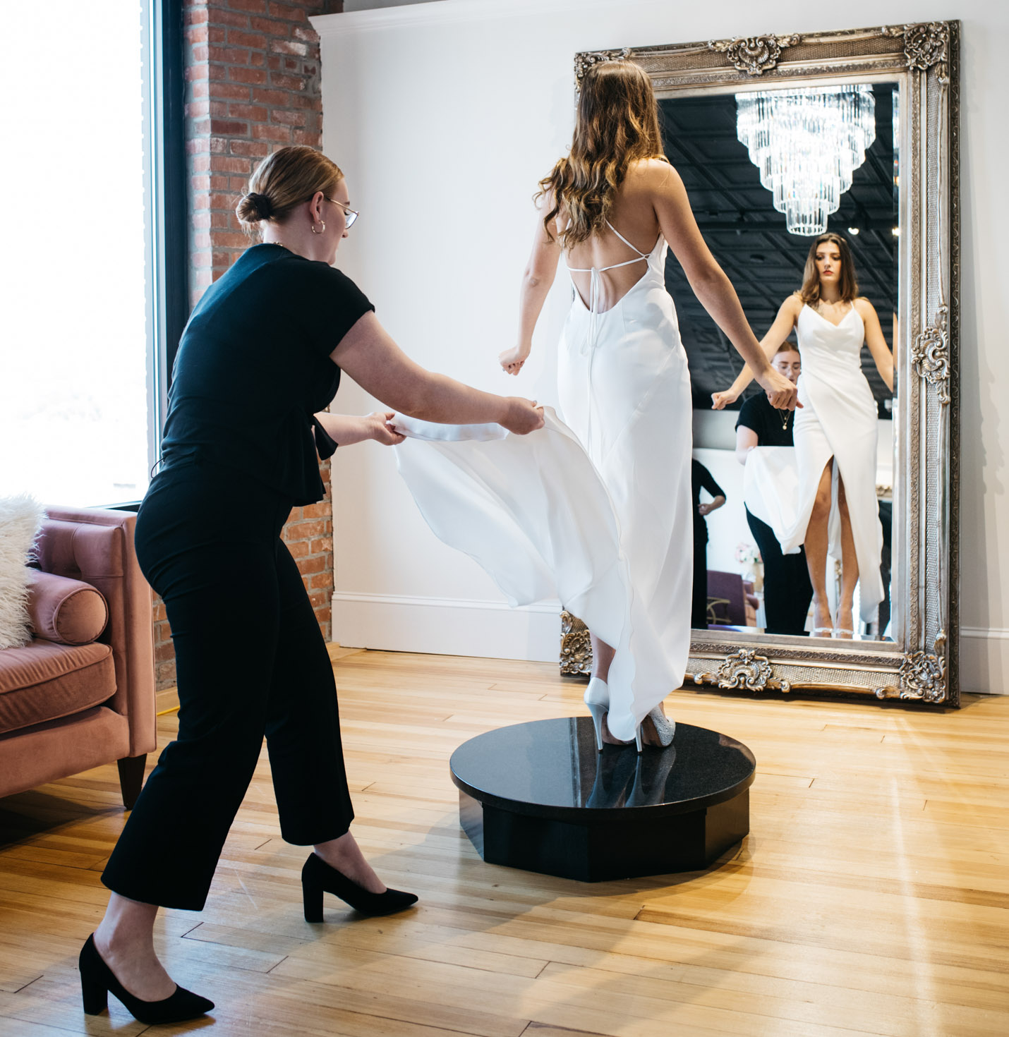 A store assistant helping a bride try on a dress.